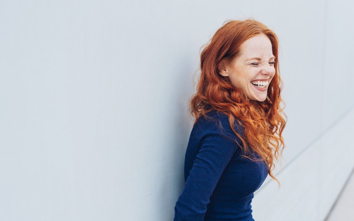 Kvinna med rött hår som står mot en vägg och ler stort