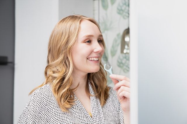 woman with white teeth flossing in mirror