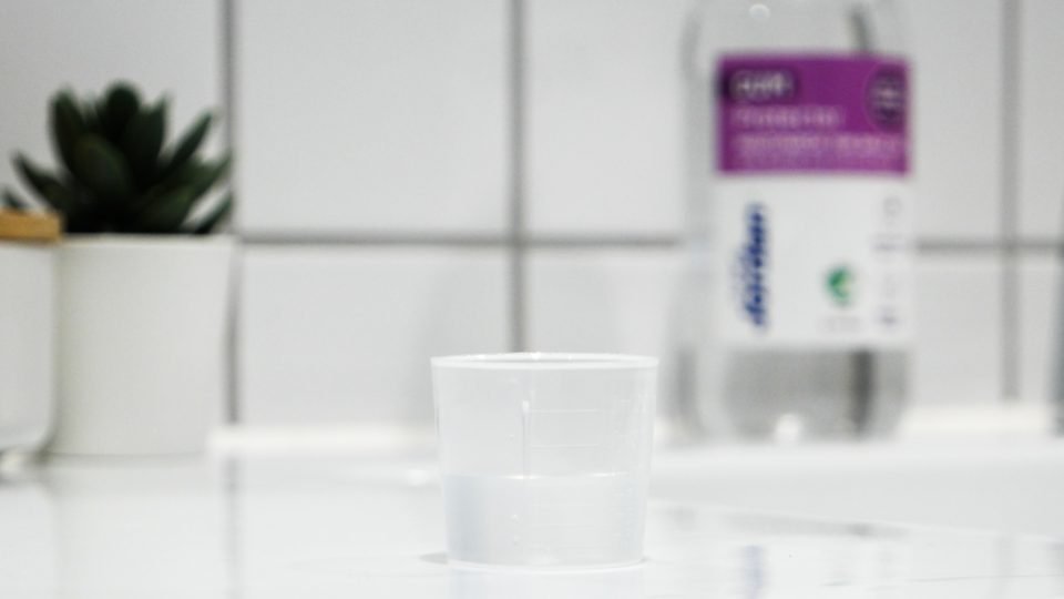 mouthwash cup on bathroom counter with mouth wash bottle in the background