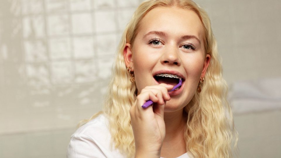 Ung person med tandställning som borstar tänderna