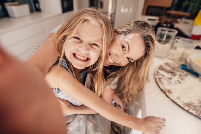 Donna bionda con bambina sorridenti si scattano un selfie sporche di farina